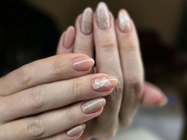 Elegant nude and glittery nail design with a white flower accent.