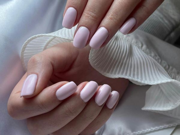 Hands with soft pink manicured nails against white fabric.