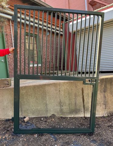 A person holding a black metal gate outdoors near a brick building.
