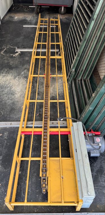 A yellow metal conveyor chain system with a motor on the side.
