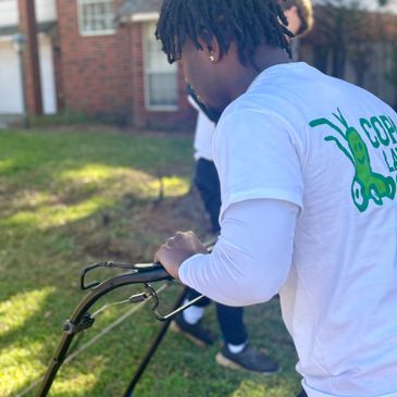 Person mowing the lawn wearing a white shirt with a green logo.