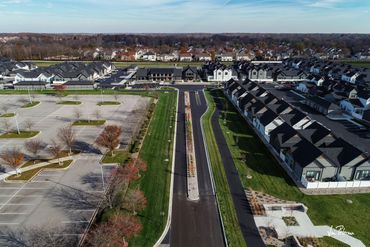 Aerial view of a suburban residential area with modern houses and empty parking lots under a clear blue sky.