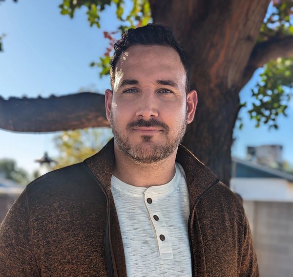 A handsome man standing in front of a tree.