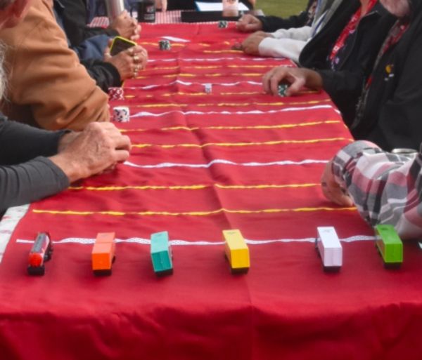 People playing a tabletop toy car racing game on a red cloth.