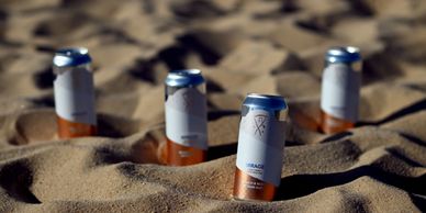 Four beverage cans partially buried in sand on a beach.