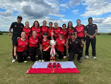 A joyful sports team posing with a trophy and flag on a grassy field under a partly cloudy sky.