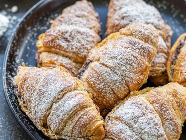 Golden croissants dusted with powdered sugar on black plates.