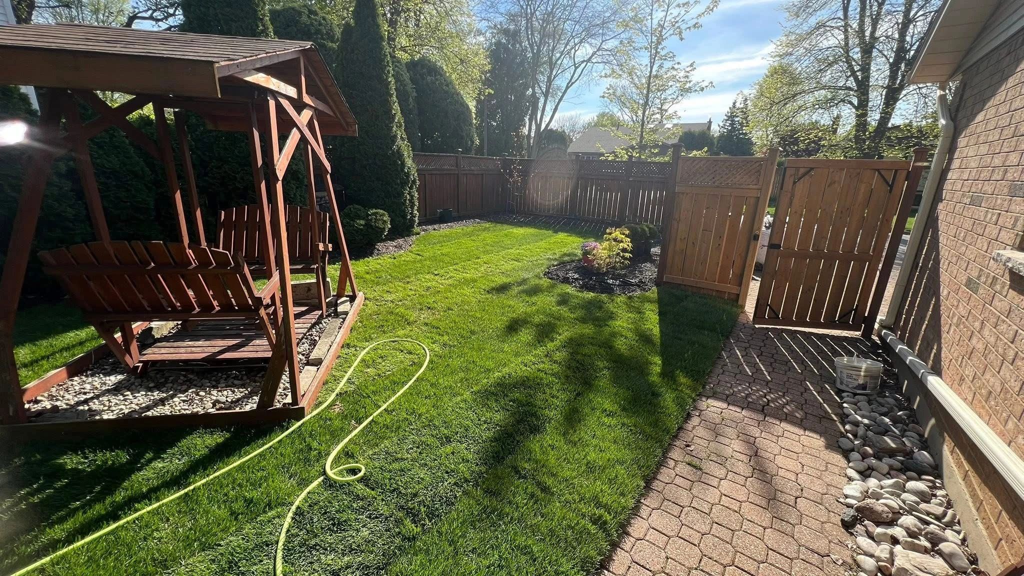 Sunny backyard with wooden swing, green lawn, and open wooden gate.