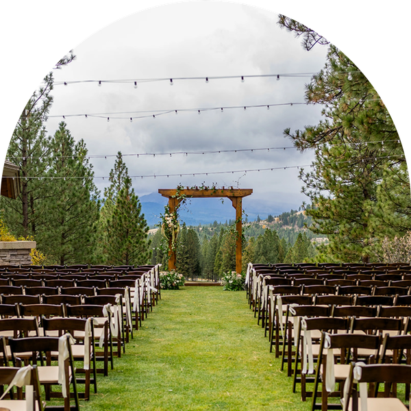 Outdoor wedding setup with wooden chairs and floral arch in a scenic forested area.