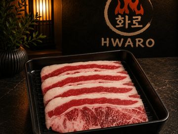 Thinly sliced marbled beef arranged in a black tray at Hwaro restaurant.