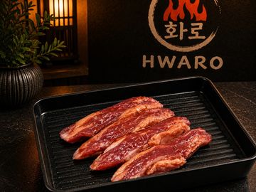 Marinated raw meat strips on a black grill pan at a restaurant.