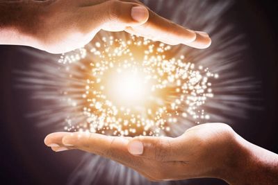 Two hands surrounding a glowing, sparkling light orb.