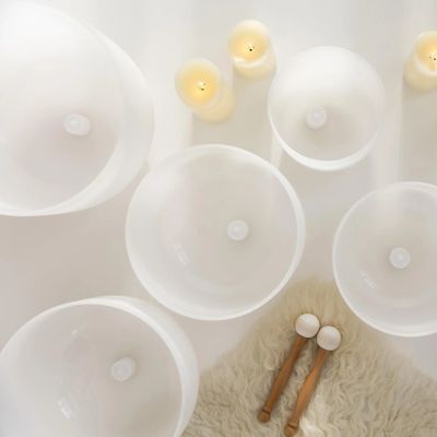 Top view of white singing bowls and candles on a soft rug.