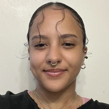 Portrait of Aliyah, a stylist, smiling with her hair slicked back, wearing a black Myrtle Beach sweatshirt.