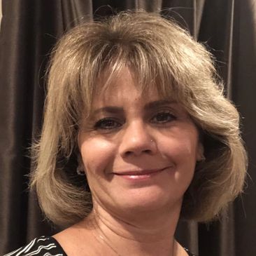 Portrait of Lisa, stylist and owner, smiling in front of a dark curtain.