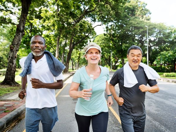 Three diverse seniors jogging happily outdoors on a sunny day.