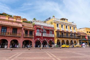Colorful colonial buildings with arches and balconies in a sunny plaza.