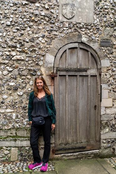 Woman standing next to an old wooden door in a stone wall.