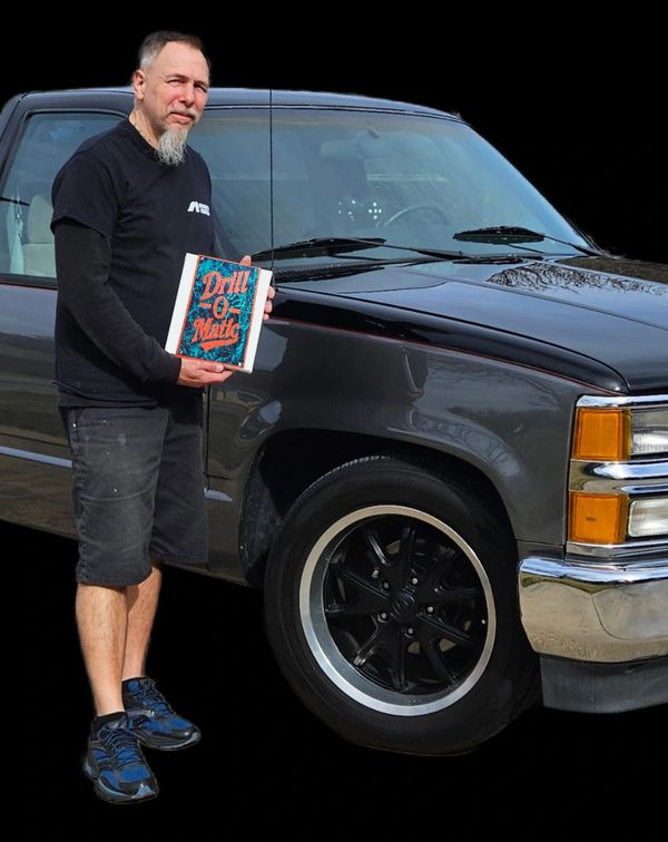 Man holding a Drill-O-Matic book beside a classic truck.