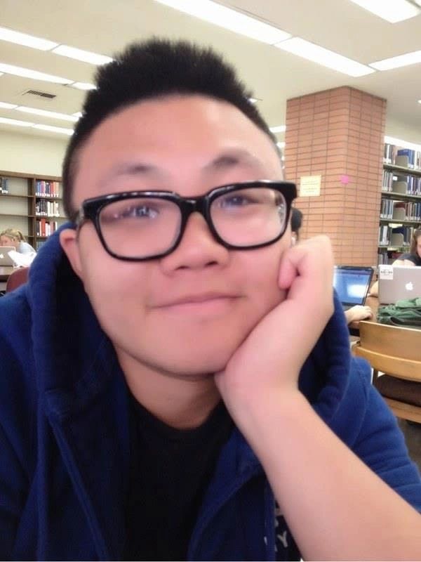 Young person with glasses resting their face on their hand in a library.