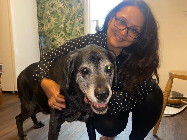 Woman smiling and hugging a large black dog indoors.