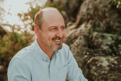 Homme souriant en extérieur avec chemise bleue.