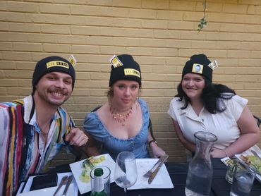 Three friends wearing matching black beanies enjoying a meal together.