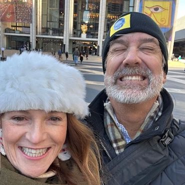 Smiling couple in winter attire enjoying a day out in front of a theater.