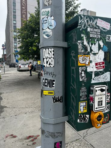 Urban street corner with various stickers on a pole and pedestrian button box.