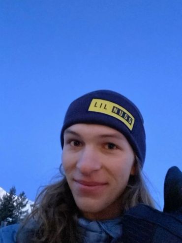 Young person smiling outdoors wearing a "LIL NUGG" beanie and giving thumbs up.