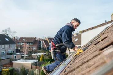 A man installing solar panels on a residential rooftop under clear sky.