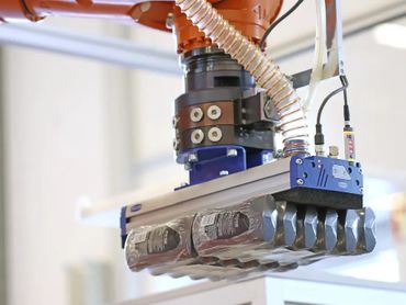 Robotic gripper handling a pack of bottled drinks in a factory setting.