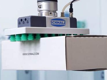 Robotic vacuum gripper lifting a white box with green suction cups.