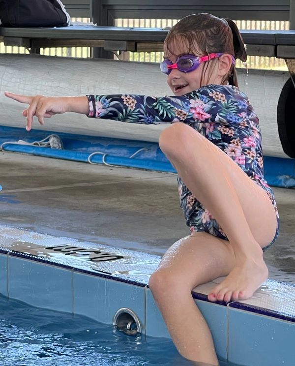 The image shows a young girl sitting on the edge of a swimming pool.
