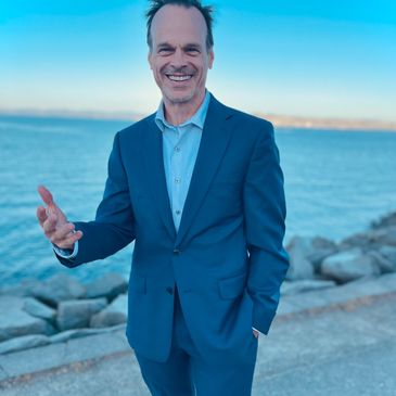 Man in blue suit smiling by the water.