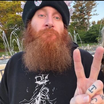 Man with a long red beard making a peace sign outdoors.