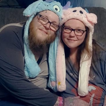 A couple wearing cute animal hats, sitting closely and smiling.