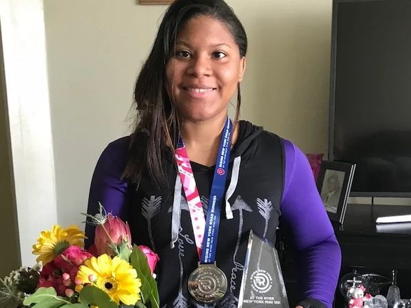 Johileny with flowers, medal and glass award. Smiles into the camera.