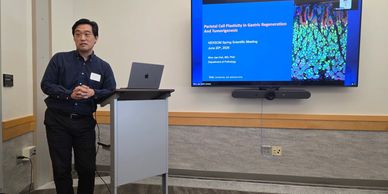A man giving a scientific presentation with slides on cell plasticity and regeneration.