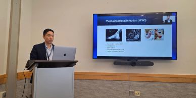 A man presenting a lecture on musculoskeletal infection with slides.