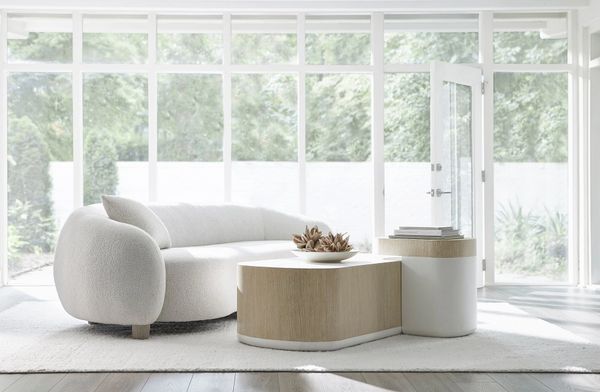 Bright living room with a curved white sofa and modern wooden coffee tables.