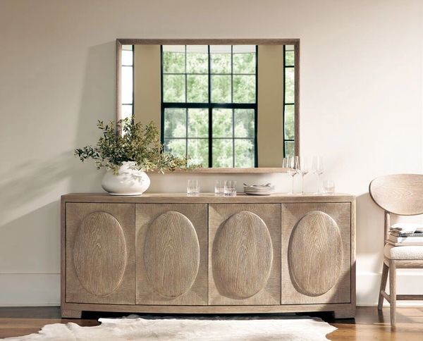 Wooden sideboard with oval patterns, mirror, and decorative items in a minimalist room.