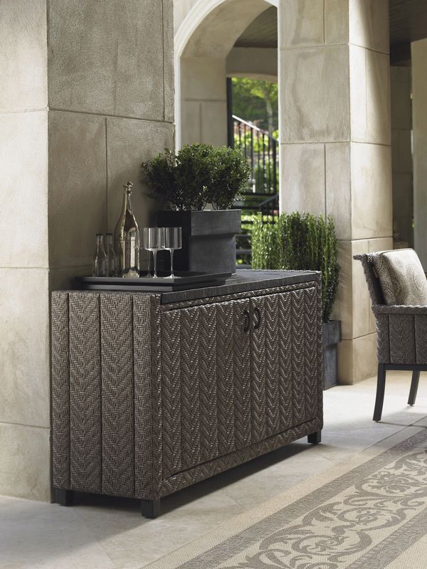 Outdoor wicker cabinet with plants and glassware in a covered patio area.