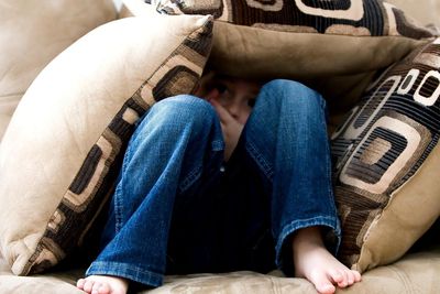 Child hiding under pillows on a sofa