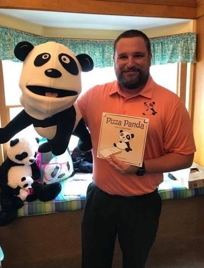 Man holding a puppet and a Pizza Panda sign, surrounded by panda-themed items.