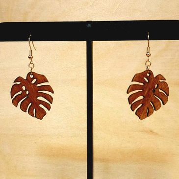 Leaf-shaped wooden earrings hanging on a black stand.
