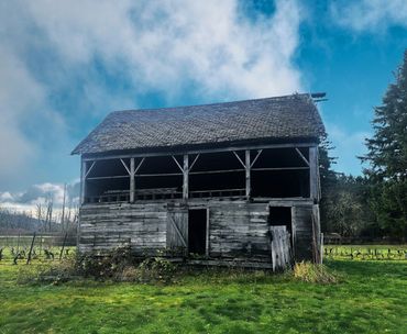 An old, weathered barn stands in a green field under a cloudy blue sky.