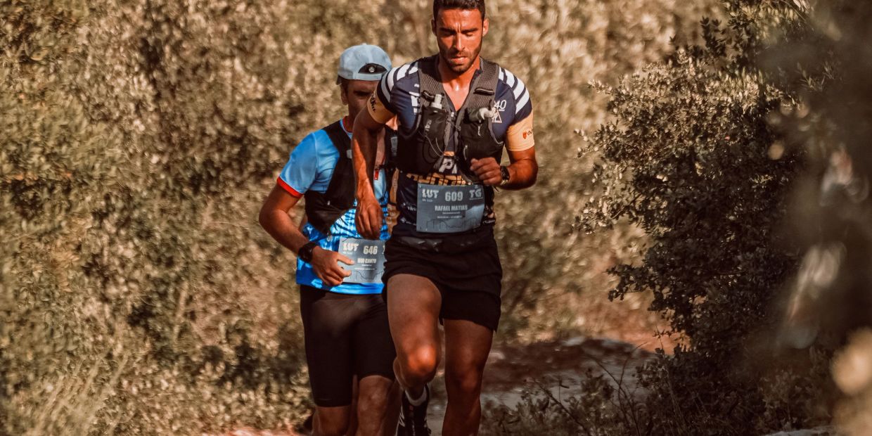 Two men running a trail race through a wooded area.