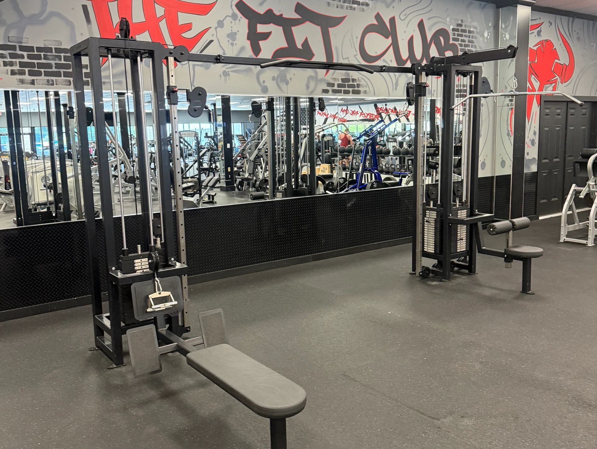 Empty gym area with cable machine and bench, graffiti wall art.