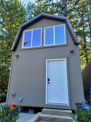 Compact tiny house with large windows in a forested area.